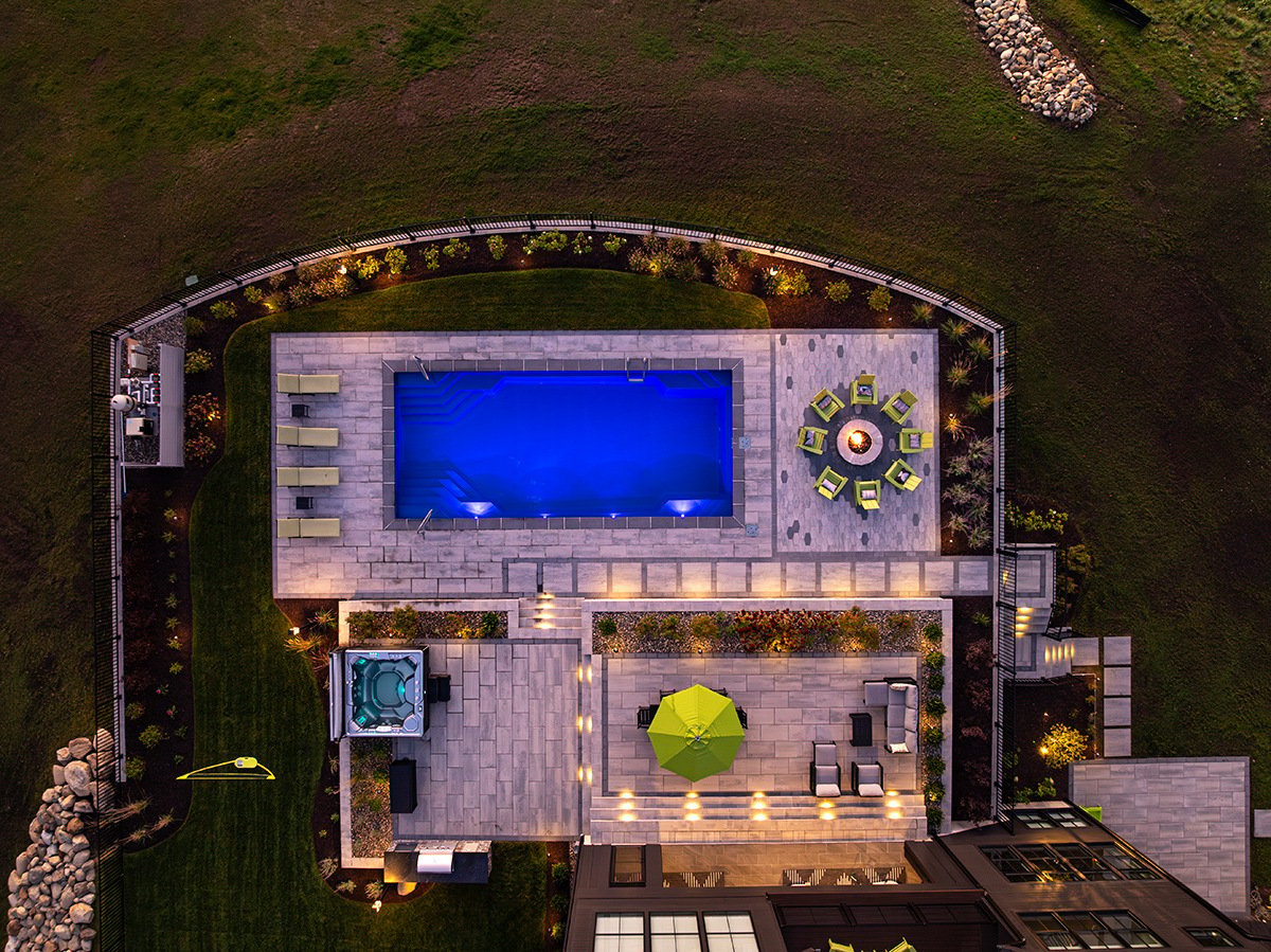 aerial view of a pool and surrounding living spaces lit up by landscape lighting fixtures