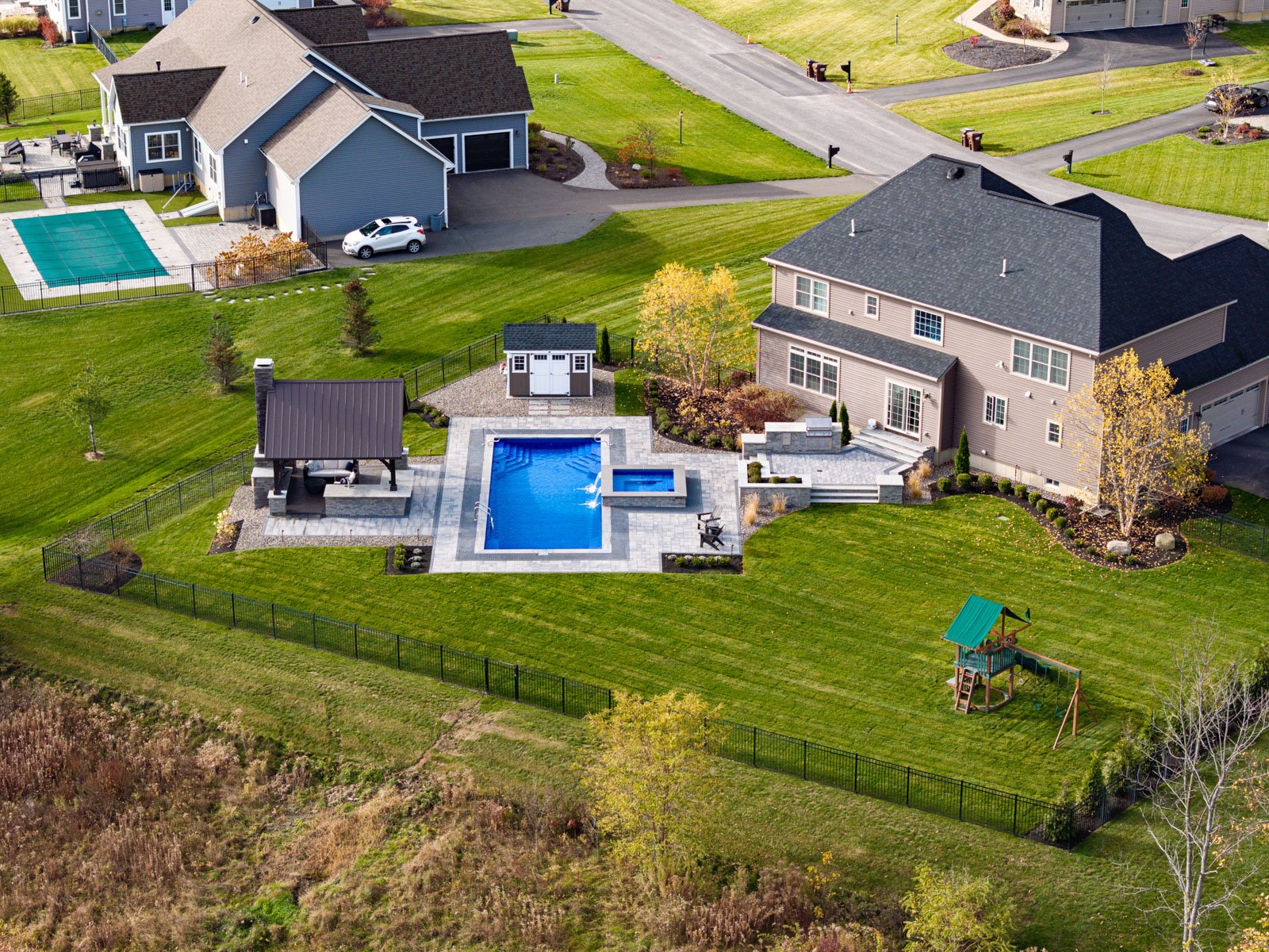 aerial view of a backyard landscape with a pool, patio, pergola, and play space