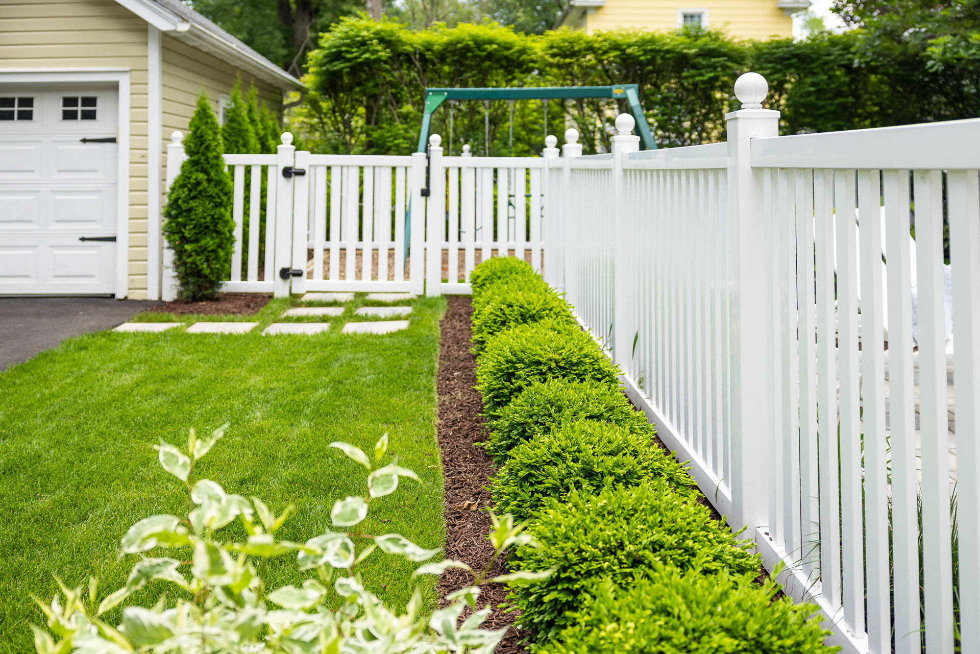 planting bed shrubs grass steppers white fence gate